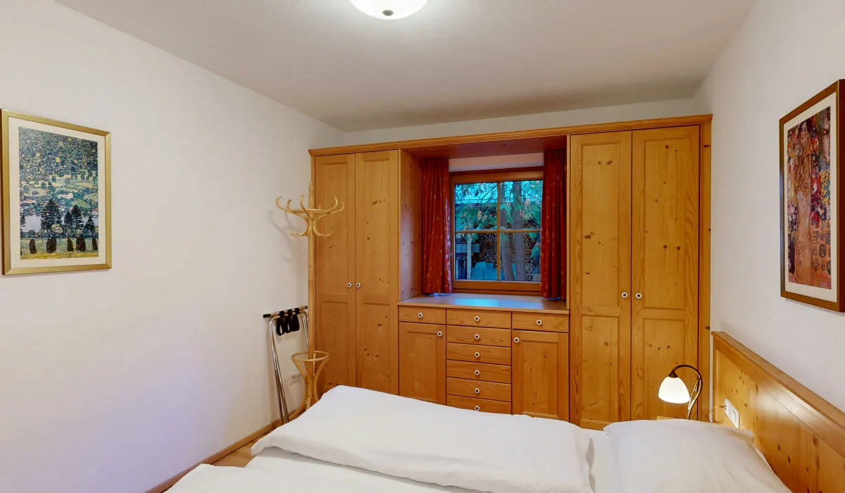 Holzmöbel und Fenster in einem hellen Schlafzimmer mit Bildern an der Wand.