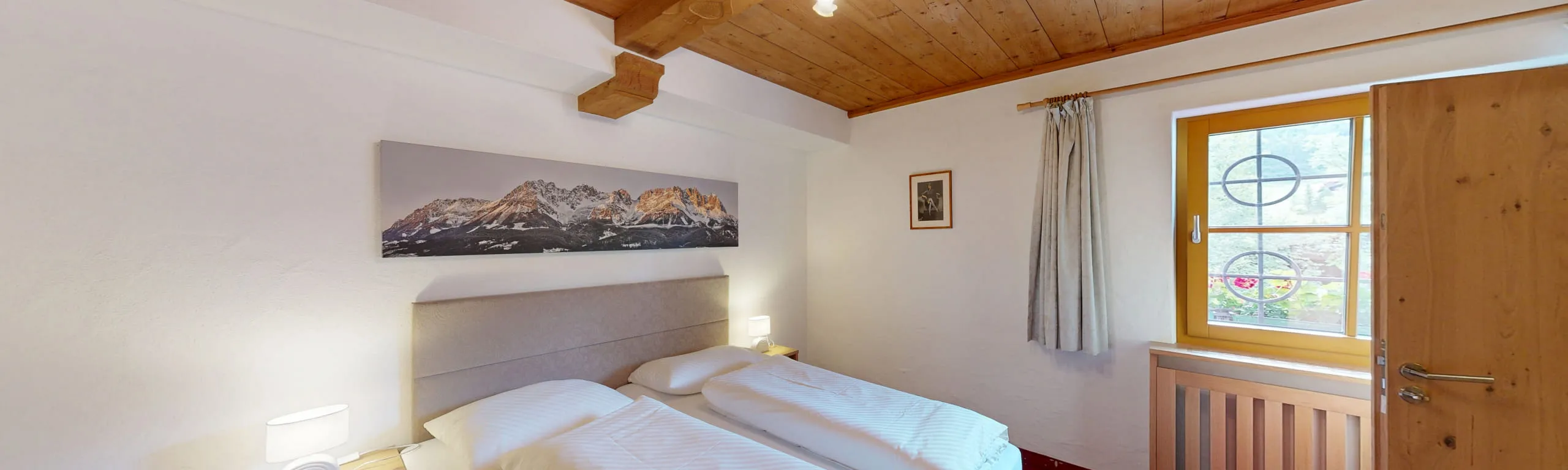 Helles Schlafzimmer mit zwei Betten, Fenster und einem Bergbild an der Wand.